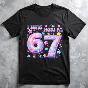 Pu&ograve; includere: T-shirt nera con la scritta "I WAS NOW I'M" sopra un grande design colorato "67". I numeri sono decorati con un effetto palla da discoteca e circondati da stelle rosa, blu e gialle.