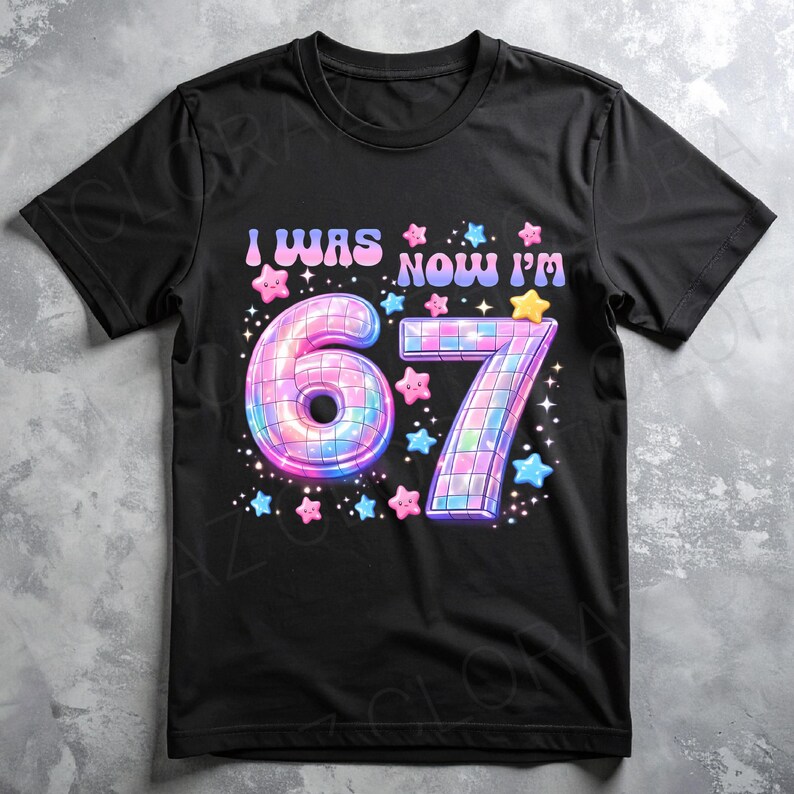 Pu&ograve; includere: T-shirt nera con la scritta "I WAS NOW I'M" sopra un grande design colorato "67". I numeri sono decorati con un effetto palla da discoteca e circondati da stelle rosa, blu e gialle.