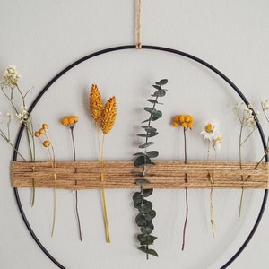 May include: A black metal hoop with a woven jute strip across the centre. Dried flowers and greenery are arranged in the hoop, including white baby's breath, yellow flowers, and green eucalyptus.