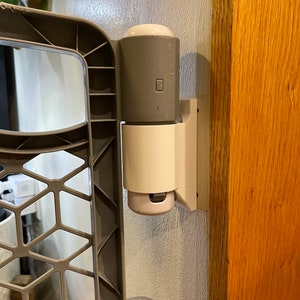 May include: A gray baby gate with a white plastic latch attached to a wooden door frame.