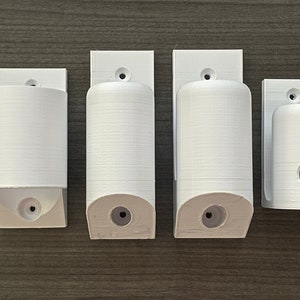 May include: Four white plastic wall mounts for holding various items. The mounts have different sizes and shapes, with some having a hole in the center.