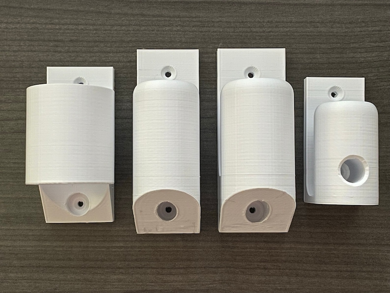 May include: Four white plastic wall mounts for holding various items. The mounts have different sizes and shapes, with some having a hole in the center.