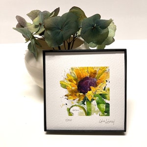 May include: A framed watercolor painting of a sunflower with yellow petals and a dark purple center. The painting is signed "Lisa LeRoy" and numbered "1/500".