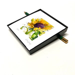 May include: A framed watercolor painting of a sunflower with a black frame. The painting is signed "Lisa Koenig" and dated "11/2021".