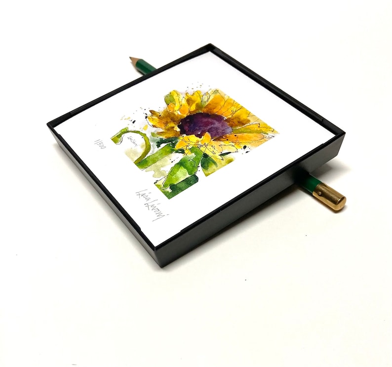 May include: A framed watercolor painting of a sunflower with a black frame. The painting is signed "Lisa Koenig" and dated "11/2021".