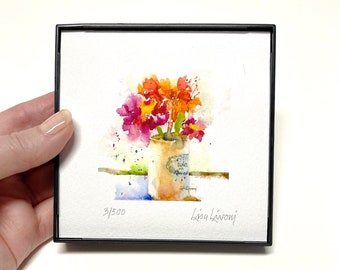 Può includere: Un dipinto ad acquerello di un mazzo di fiori rosa, arancioni e gialli in un vaso di ceramica bianco con un'etichetta blu. Il dipinto è firmato "Lisa Livoni" e numerato "3/500".