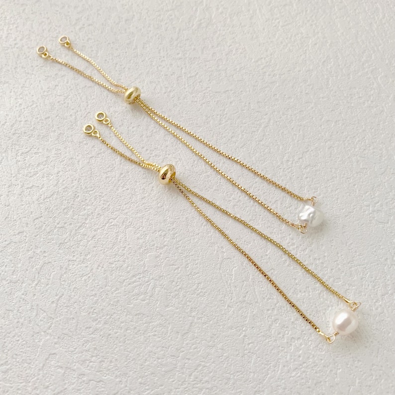 Pu&ograve; includere: Tre braccialetti a catena dorati con nodi scorrevoli regolabili e accenti di perle. Le perle sono di diverse dimensioni e forme.