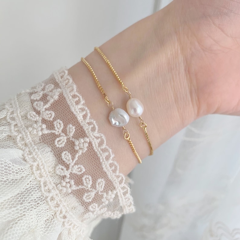 Pu&ograve; includere: Due braccialetti a catena dorata con accenti di perle. I braccialetti sono delicati e presentano un'unica perla su ogni catena.