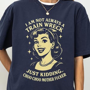 May include: Navy blue t-shirt with a retro illustration of a woman and the text "I AM NOT ALWAYS A TRAIN WRECK JUST KIDDING.. CHOO CHOO MOTHER FUCKER" in a vintage style. The shirt has short sleeves and a relaxed fit.