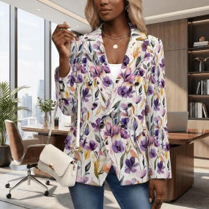 May include: A double-breasted blazer with a floral pattern in shades of purple, pink, and yellow on a white background. The blazer has black buttons and long sleeves. A white handbag with a shoulder strap is also visible.