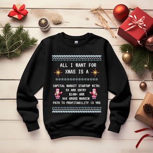 Peut inclure: Un sweat-shirt noir à manches longues avec une impression graphique blanche portant le texte : ALL I WANT FOR XMAS IS A CAPITAL MARKET STARTUP WITH: 5X ARR ENTRY $10M+ ARR 80% GROSS MARGIN PATH TO PROFITABILITY < 3 YRS, encadré par deux petits pères Noël.