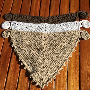 Puede incluir: Tres bufandas triangulares de ganchillo en marr&oacute;n, blanco y beige con bordes decorativos de ganchillo y un bot&oacute;n en cada extremo.
