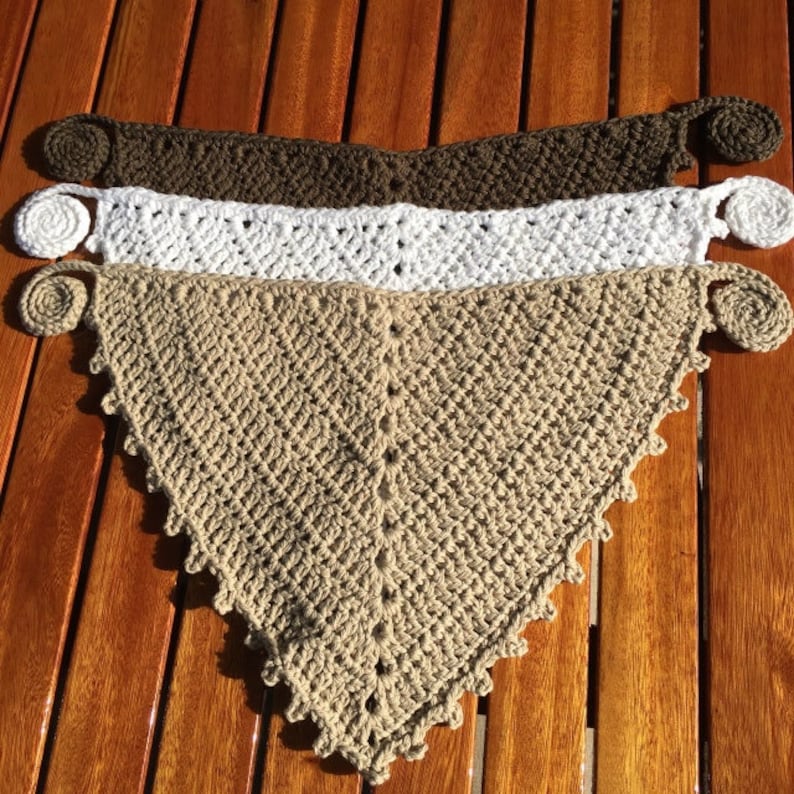 Puede incluir: Tres bufandas triangulares de ganchillo en marr&oacute;n, blanco y beige con bordes decorativos de ganchillo y un bot&oacute;n en cada extremo.