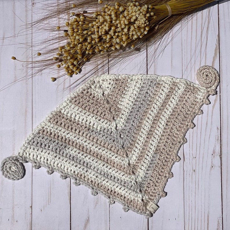 Puede incluir: Un gorro de punto de tri&aacute;ngulo con un patr&oacute;n de rayas en beige, blanco y gris. El gorro tiene un pomp&oacute;n de punto en cada esquina.