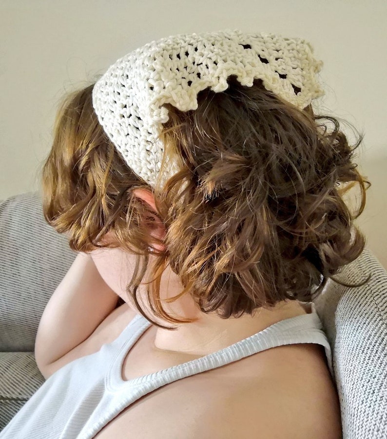 Puede incluir: Una diadema de crochet blanca con un borde festoneado. La diadema est&aacute; puesta en una persona con el pelo rizado marr&oacute;n.