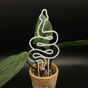 May include: White metal snake plant stake, shaped like a snake, in a terracotta pot with a green plant.