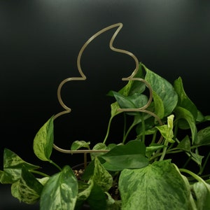 May include: A gold metal plant stand shaped like a poop emoji. The stand is surrounded by a potted plant with green and white variegated leaves.