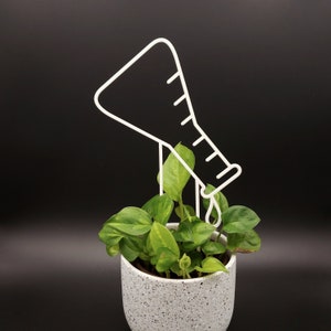 May include: White metal plant watering device shaped like a beaker pouring water onto a potted plant with green leaves.