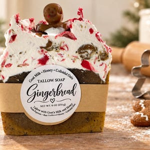 May include: A rectangular bar of Gingerbread tallow soap topped with white frosting, red accents, and a small gingerbread man figure. A tan paper label features the text "Tallow Soap Gingerbread" and "Net Wt. 6 oz (170 g)" with goat milk, honey, and colloidal oats.