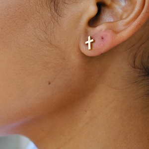 May include: A close-up of a person's ear with a small gold cross earring.