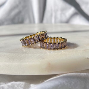 May include: Two gold rings with a row of purple baguette-shaped stones.