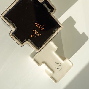 May include: Two ceramic pieces, one black and one white, with a unique T-shaped design. The black piece has the text "1013/G ITALY" in orange. The white piece has the text "1012/P ITALY" in black.