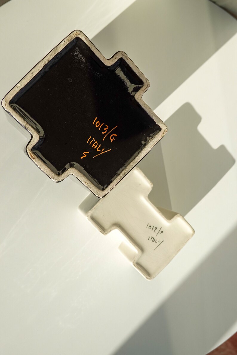 May include: Two ceramic pieces, one black and one white, with a unique T-shaped design. The black piece has the text "1013/G ITALY" in orange. The white piece has the text "1012/P ITALY" in black.