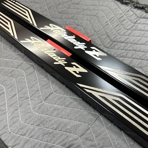 May include: Pair of black Fairlady Z rocker panels with white and silver accent stripes and red mounting tabs. The panels are angled and have the Fairlady Z logo in white script.