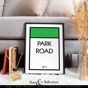 Könnte beinhalten: Ein gerahmter Druck mit einem grün-weißen Design, das die Worte "PARK ROAD" in Schwarz zeigt. Die Nummer "Nº7" befindet sich unter dem Text. Der Druck befindet sich auf einem weißen Teppich, mit einem grauen Sofa im Hintergrund. Der untere Teil des Drucks lautet "Hues & Reflections".