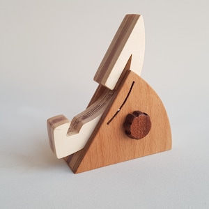 Op de afbeelding: Een houten telefoonstandaard met een wit en bruin gestreept ontwerp. De standaard heeft een kleine knop aan de zijkant.