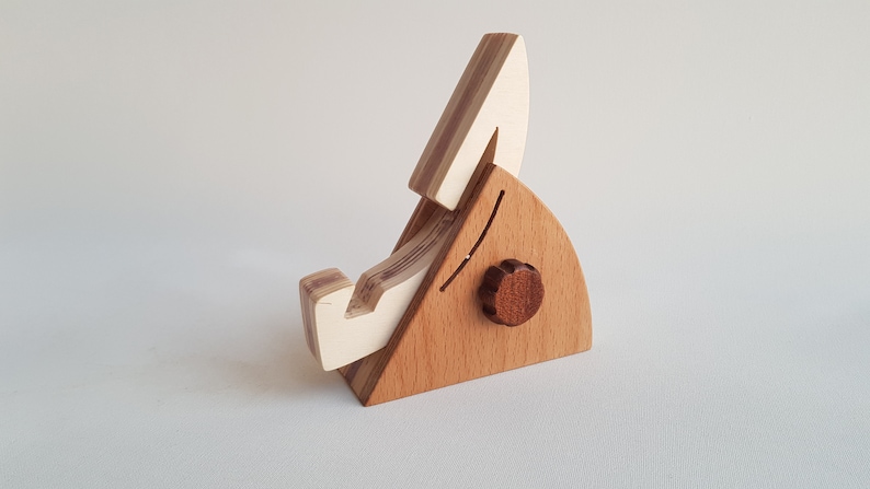 Op de afbeelding: Een houten telefoonstandaard met een wit en bruin gestreept ontwerp. De standaard heeft een kleine knop aan de zijkant.