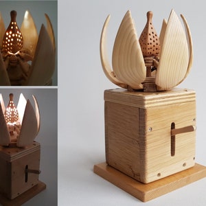 May include: A wooden sculpture of a flower with a light inside. The flower is made of multiple pieces of wood and has a small, round light in the centre. The flower is sitting on a wooden base with a lever on the side.