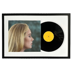 May include: A black framed picture with a black vinyl record on the right side and a photo of a woman with blonde hair on the left side. The record label is yellow with black text.
