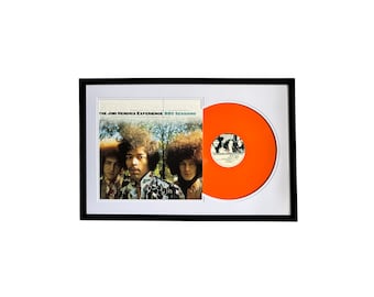 May include: A framed record album with a black frame and a white mat. The album cover features a photo of Jimi Hendrix and the Jimi Hendrix Experience. The album title is "The Jimi Hendrix Experience BBC Sessions". The record is orange.