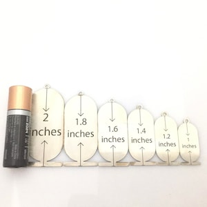 May include: Set of seven silver metal circles with arrows pointing down and measurements in inches: 2, 1.8, 1.6, 1.4, 1.2, and 1.