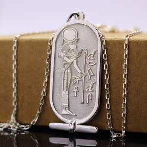 May include: Silver pendant necklace featuring an Egyptian goddess with a winged sun disk, an ankh, and other hieroglyphs. The pendant is attached to a silver chain.