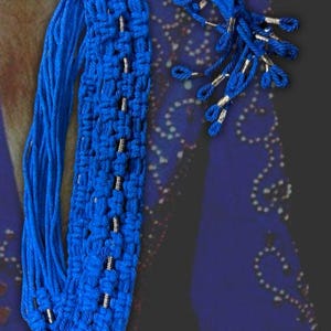 Puede incluir: Un cordón de macramé azul con cuentas plateadas. El cordón está trenzado y tiene una franja en el extremo.