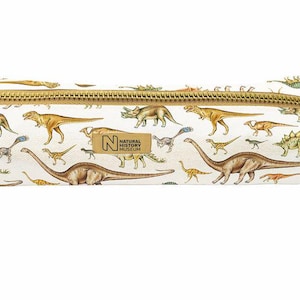 May include: A rectangular pencil case with a white background featuring a colourful dinosaur pattern. The case has a gold-toned metal zip and a small rectangular patch with the text Natural History Museum centred on the front side.