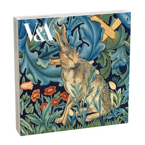 May include: A square box set titled Tapestry Wildlife featuring the V&A logo. The cover displays a brown hare sitting among blue acanthus leaves and small red and white flowers on a dark blue background. The box contains notecards with envelopes.