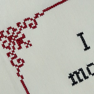 A close up photo of maroon cross stitch border and black text on white fabric.
