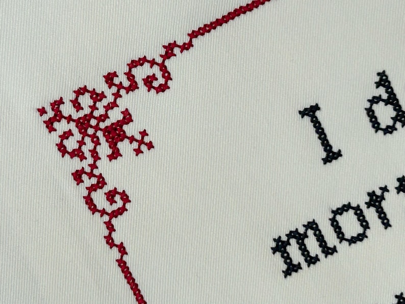 A close up photo of maroon cross stitch border and black text on white fabric.