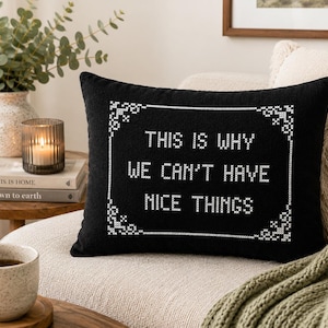 May include: A rectangular black throw pillow featuring white cross-stitch embroidery. The design includes a decorative border and the text "THIS IS WHY WE CAN'T HAVE NICE THINGS" centered in the middle, mimicking a traditional sampler style.