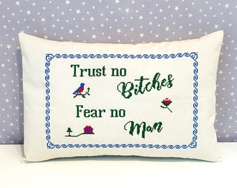 May include: Cream-colored rectangular pillow with a cross-stitched design. The text "Trust no Bitches Fear no Man" is embroidered in green, with blue and red accents. A blue border frames the text.