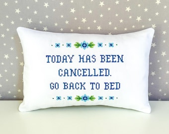 May include: White pillow with blue embroidery that reads "Today has been cancelled. Go back to bed."  The embroidery is surrounded by green and blue floral designs.