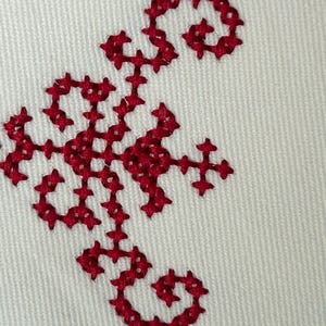 A close up photo of maroon cross stitch border on white fabric.