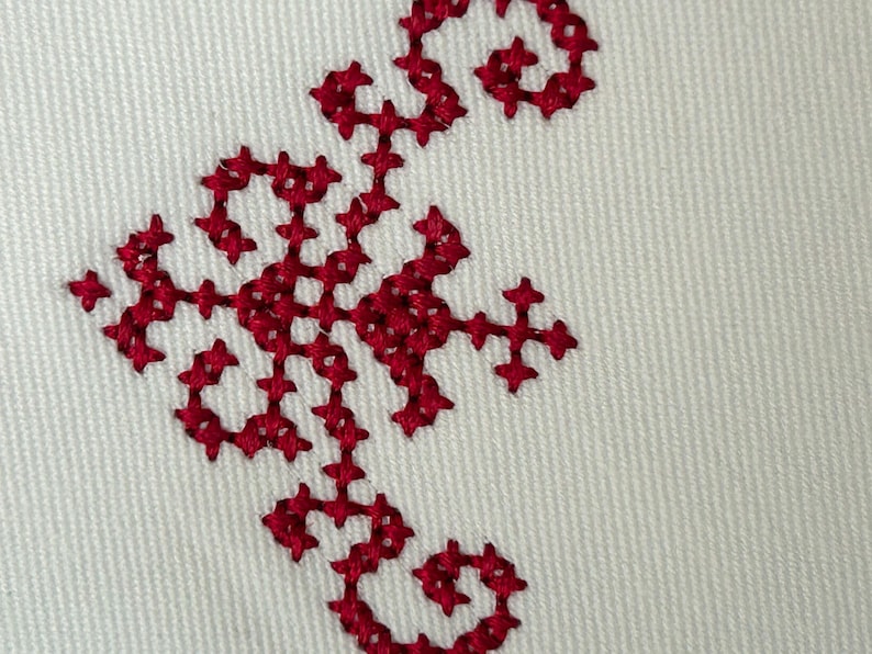 A close up photo of maroon cross stitch border on white fabric.