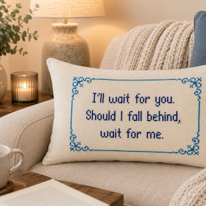 May include: A rectangular off-white throw pillow featuring blue cross-stitch embroidery. The design includes a decorative border and the text: I'll wait for you. Should I fall behind, wait for me. The pillow is made of a woven fabric material.