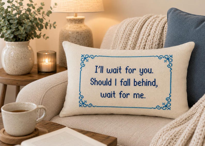 May include: A rectangular off-white throw pillow featuring blue cross-stitch embroidery. The design includes a decorative border and the text: I'll wait for you. Should I fall behind, wait for me. The pillow is made of a woven fabric material.