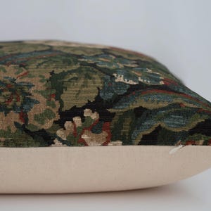 May include: Decorative pillow with a floral pattern in shades of green, brown, and blue on a black background. The pillow has a cream-colored base and a zipper closure. The pillow is designed for home decor.