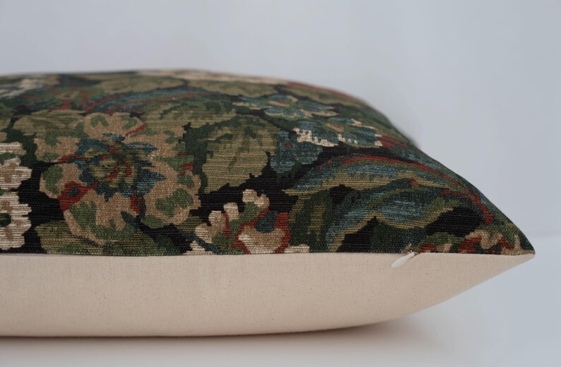 May include: Decorative pillow with a floral pattern in shades of green, brown, and blue on a black background. The pillow has a cream-colored base and a zipper closure. The pillow is designed for home decor.